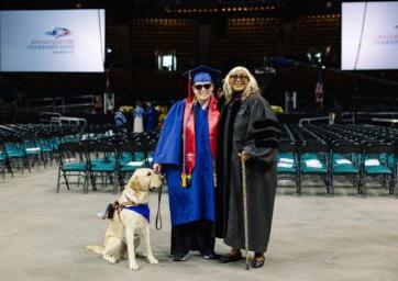 Dawn Bookhardt standing with a visually-impaired student and his dog at commencement in May 2023